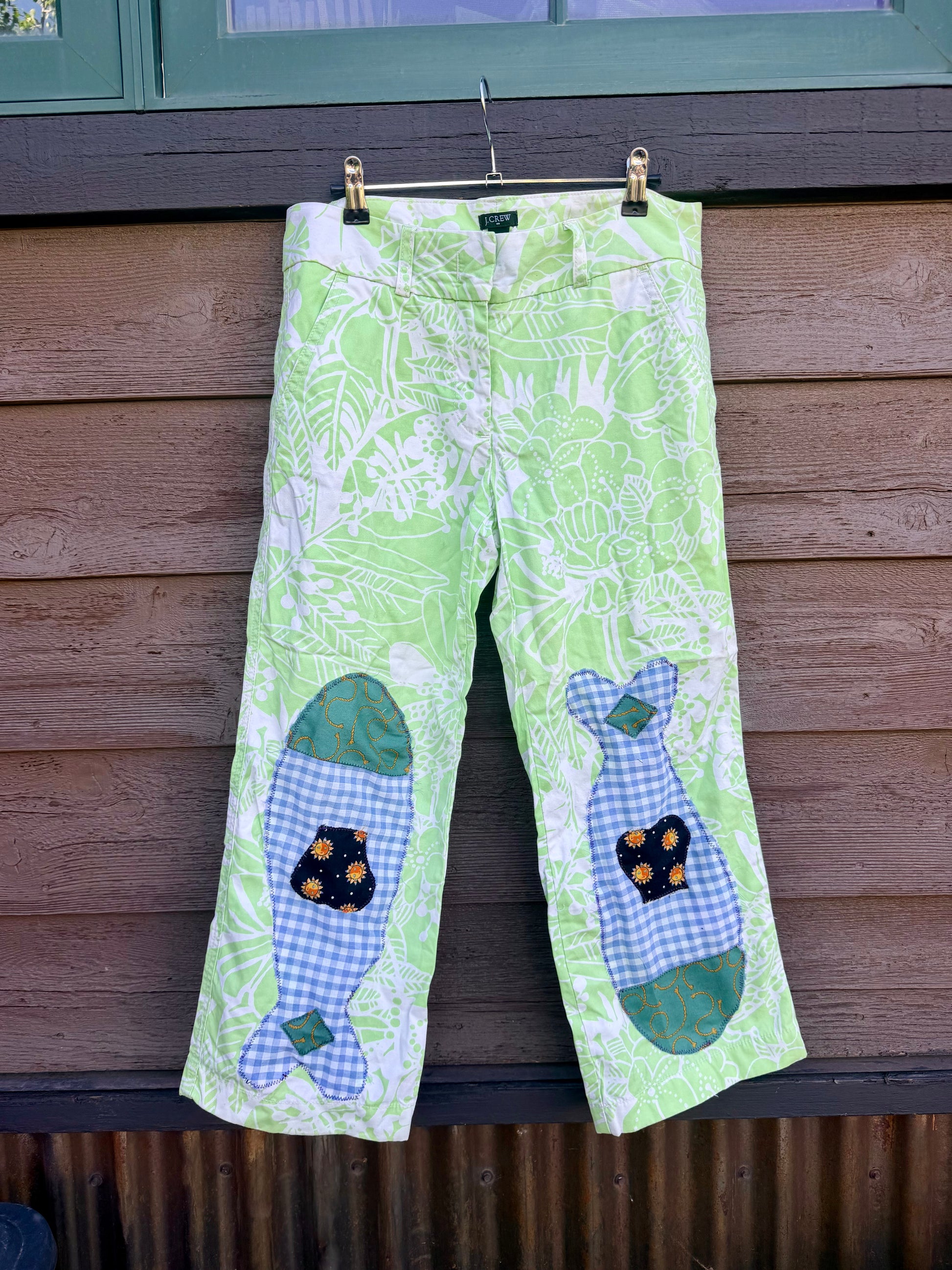 Each fish is pieced together from fabric scraps — blue gingham, teal scroll print, and a navy sun-print cotton — and stitched down with visible decorative stitching that celebrates the handmade process. The matching fish on each leg give them a playful, intentional look that’s anything but ordinary.