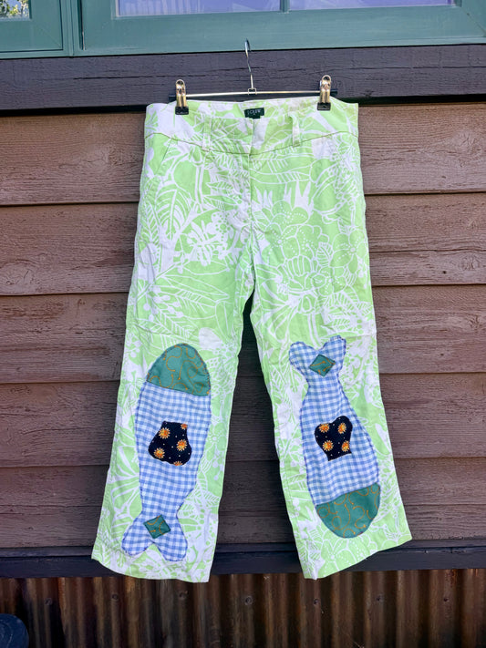 Each fish is pieced together from fabric scraps — blue gingham, teal scroll print, and a navy sun-print cotton — and stitched down with visible decorative stitching that celebrates the handmade process. The matching fish on each leg give them a playful, intentional look that’s anything but ordinary.