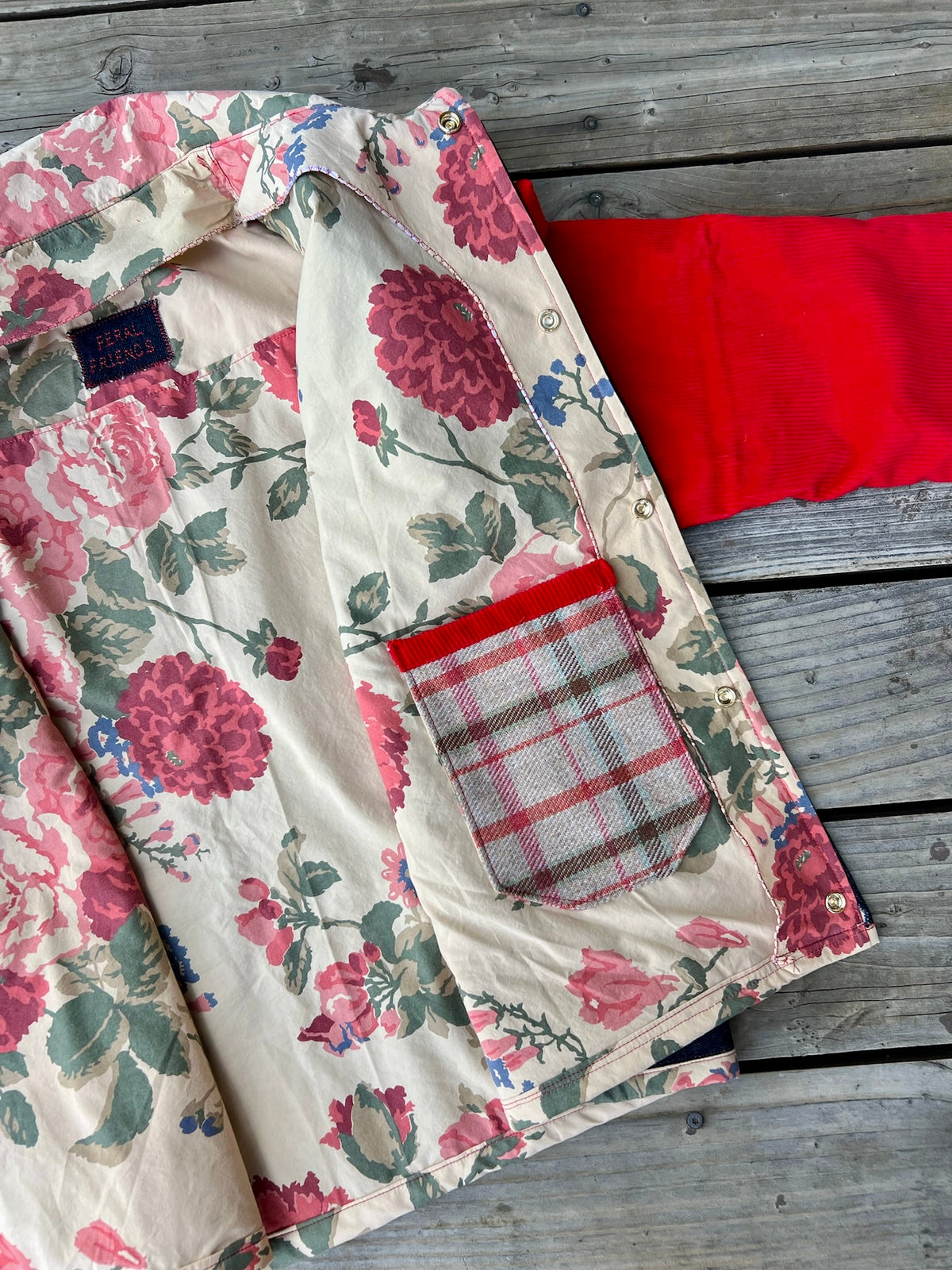 Close up of inside the denim barn coat with red corduroy sleeves showing the floral bedsheet lining and plaid pocket