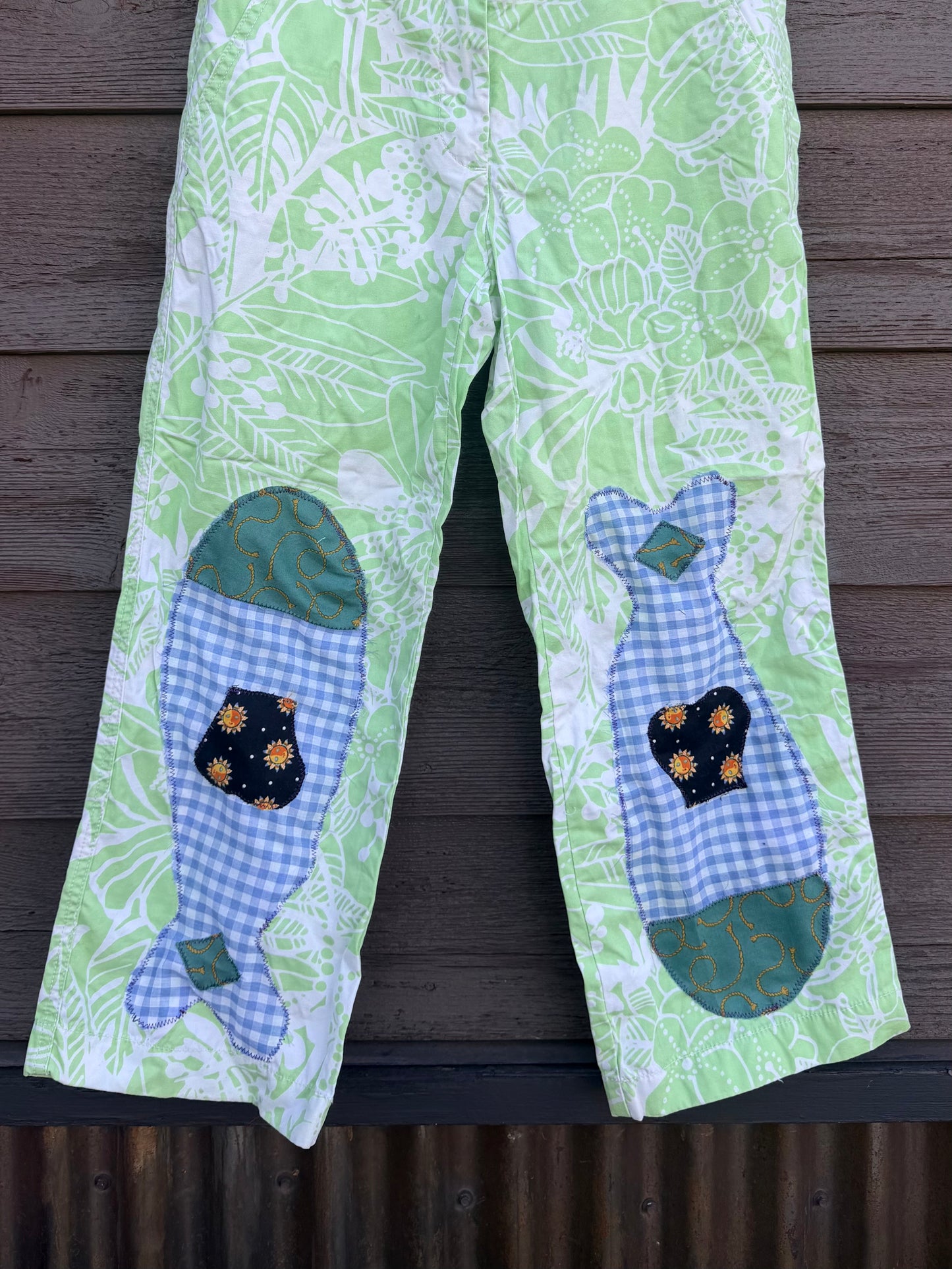 Each fish is pieced together from fabric scraps — blue gingham, teal scroll print, and a navy sun-print cotton — and stitched down with visible decorative stitching that celebrates the handmade process. The matching fish on each leg give them a playful, intentional look that’s anything but ordinary.