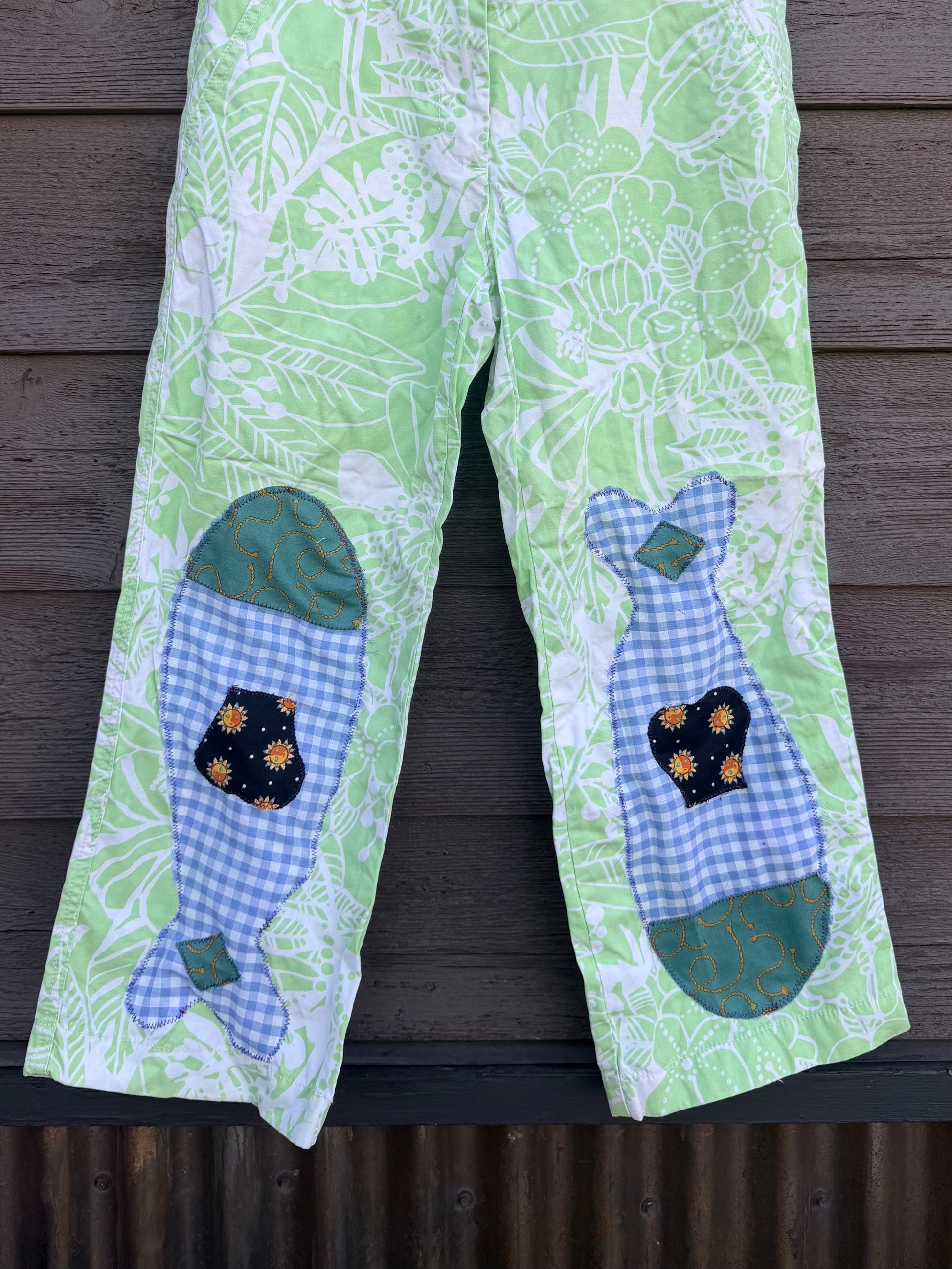 Each fish is pieced together from fabric scraps — blue gingham, teal scroll print, and a navy sun-print cotton — and stitched down with visible decorative stitching that celebrates the handmade process. The matching fish on each leg give them a playful, intentional look that’s anything but ordinary.
