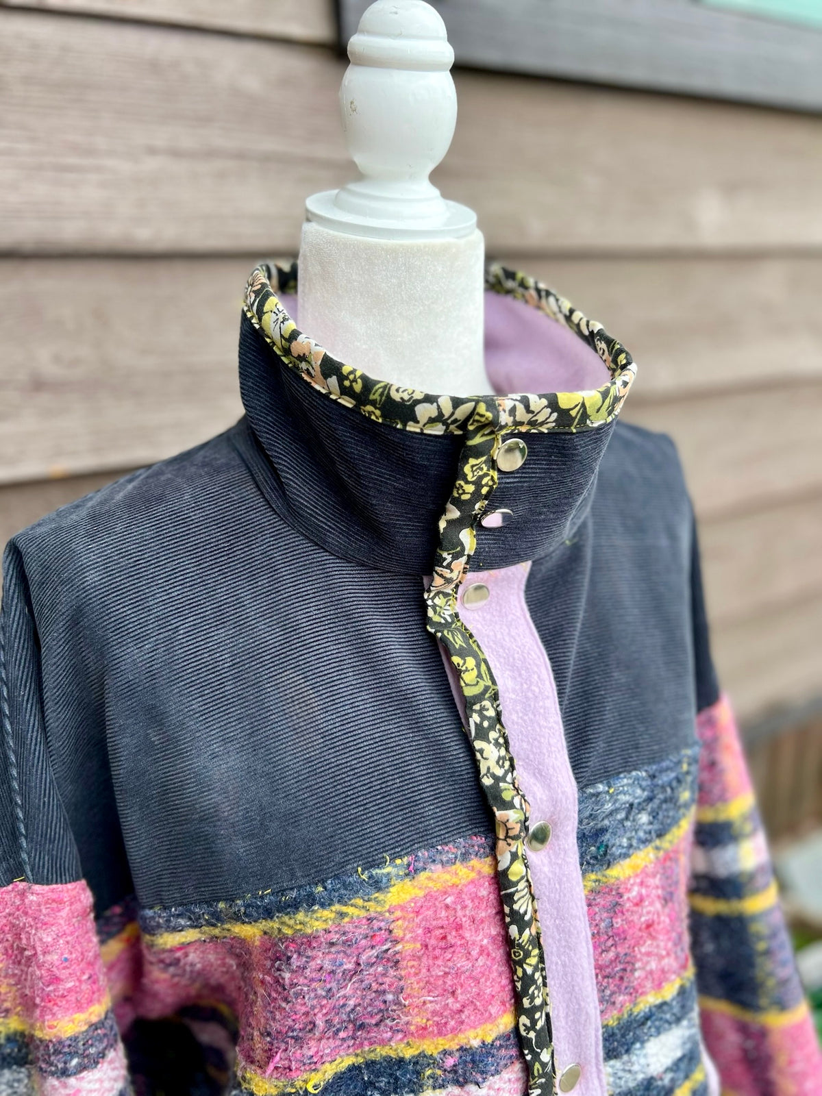 Close-up of the high corduroy collar with floral trim and snaps, shown standing up on the pink plaid blanket coat