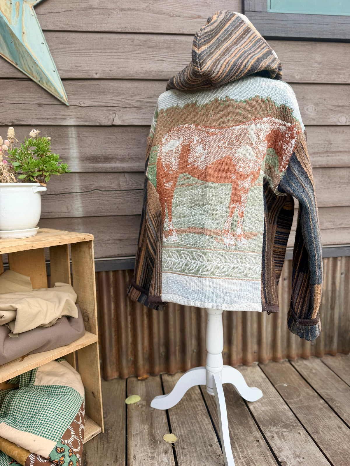 Back of the horse blanket hooded coat on a mannequin showing the woven horse blanket panel with a horse and the striped hood