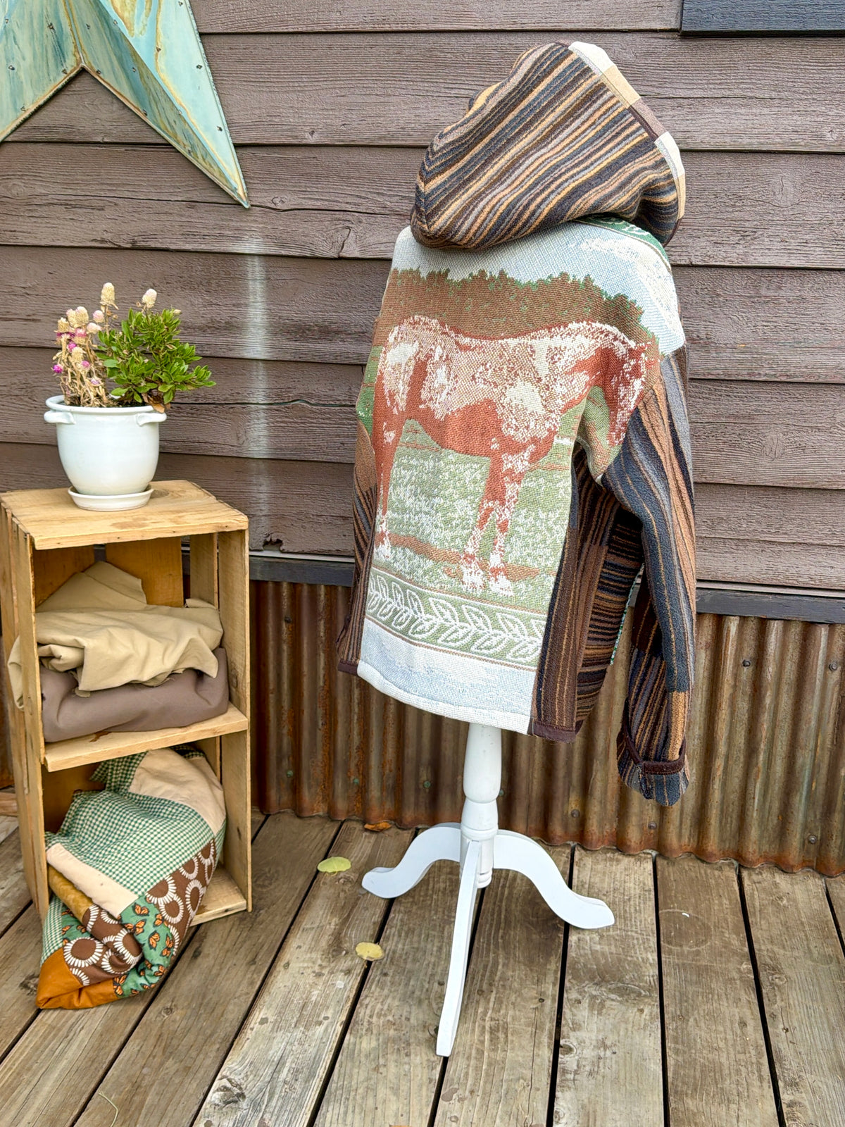 Back side of the horse blanket hooded coat on a mannequin showing the woven horse blanket panel with a horse and the striped hood