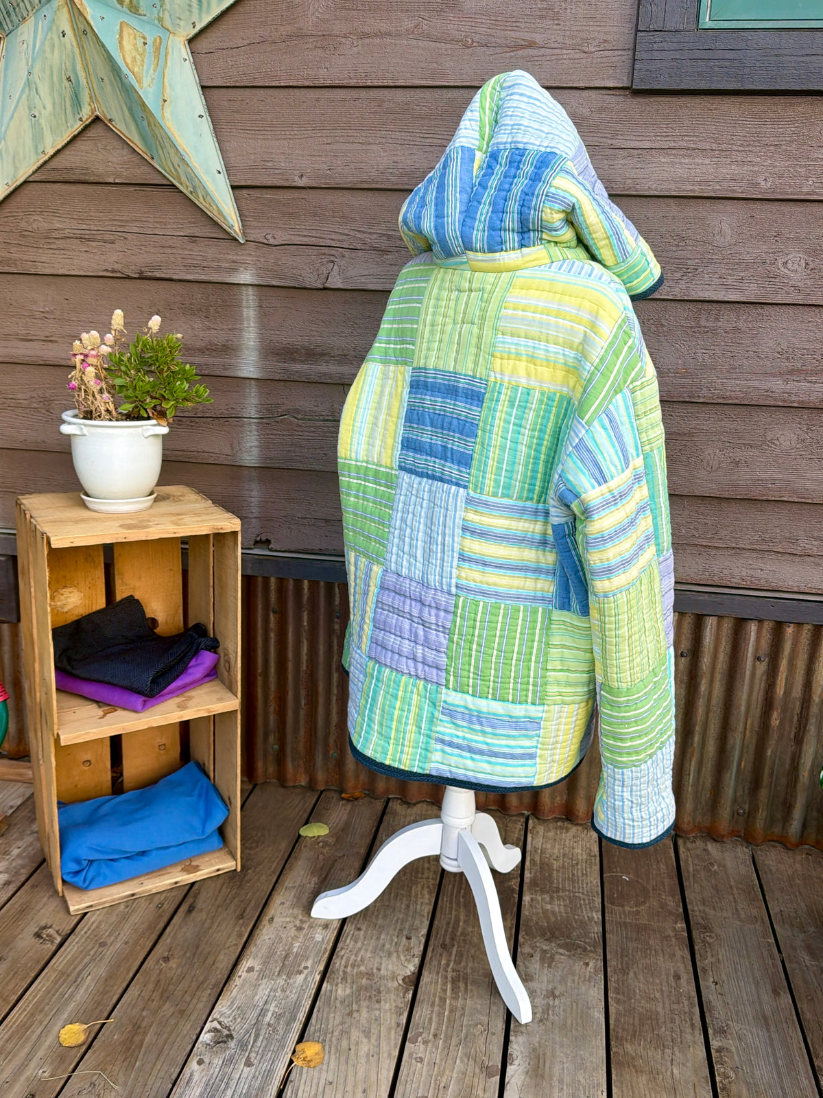 Back of the striped quilt hooded coat in green, yellow, blue and purple on a mannequin showing the quilted back and hood