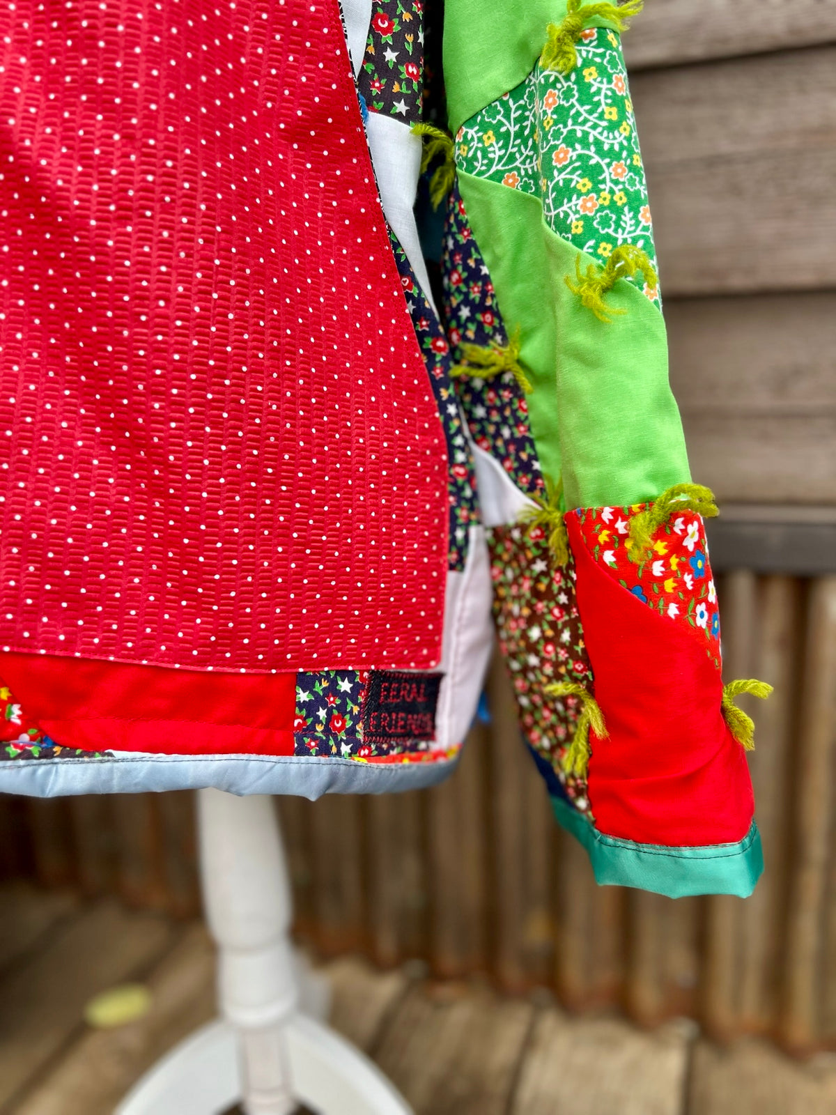 Close-up of vintage patchwork quilt with small blue yarn ties on the vintage patchwork quilt camp coat with red collar
